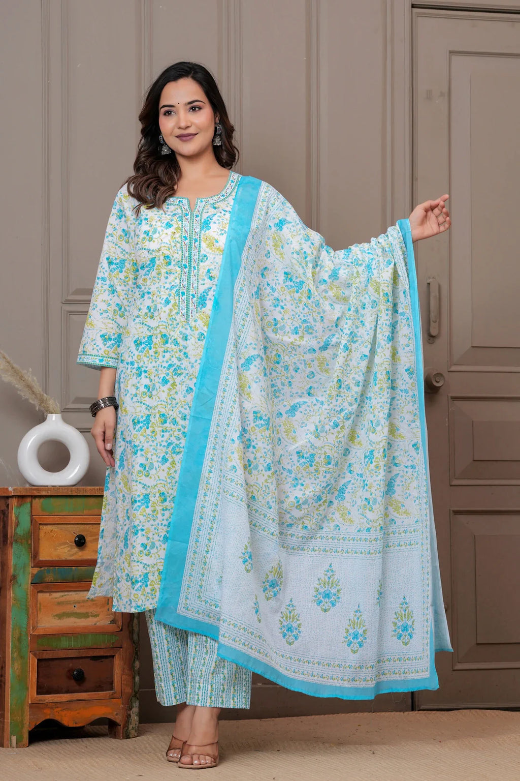 A woman posing in a white cotton kurta set featuring blue and yellow handblock floral prints with a matching dupatta and pants.