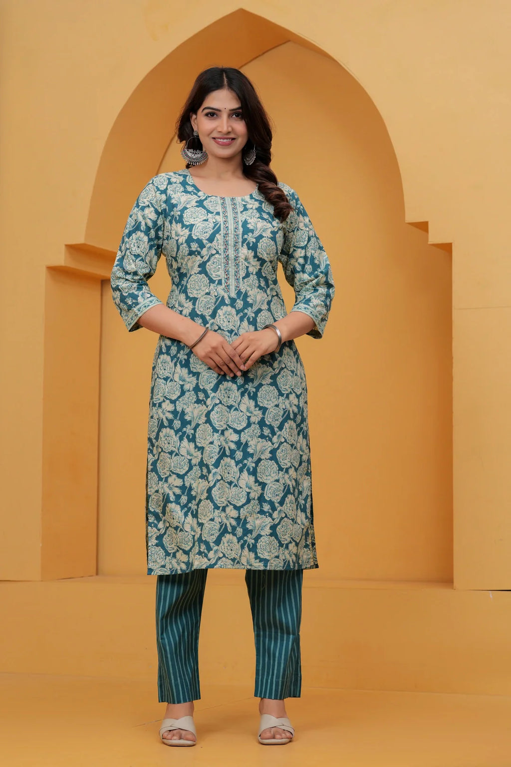 A woman wearing a teal blue cotton kurta with off-white floral handblock prints and teal vertical striped pants.