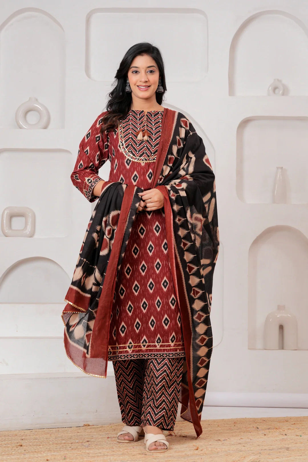 Woman wearing a maroon and black Ikat print cotton kurta set with a matching black dupatta and chevron trousers.